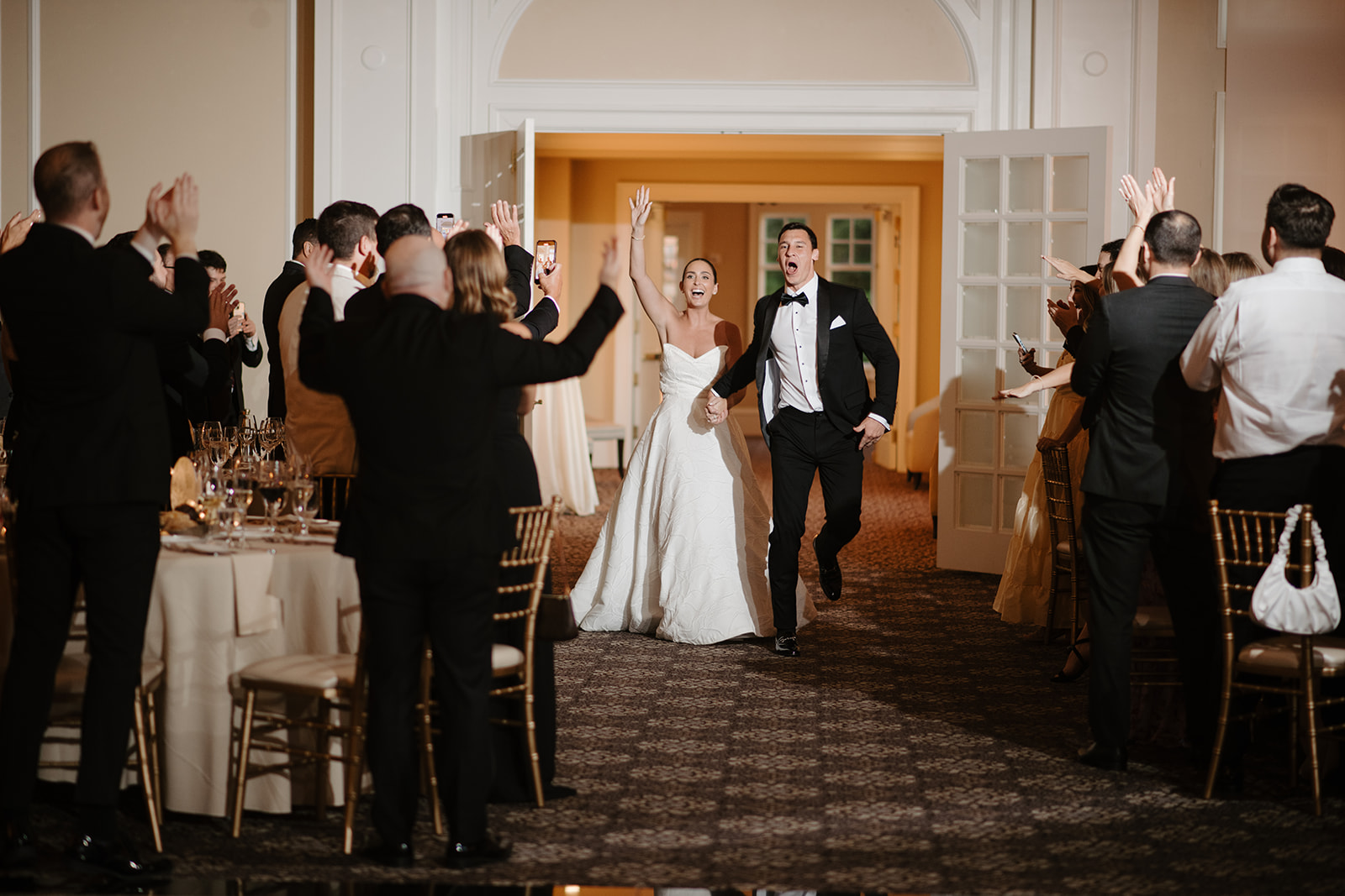 Bride and groom making a high-energy grand entrance into their reception hall, cheered on by applauding guests.